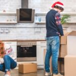 Um casal com gorros natalinos em meio a caixas, fazendo uma mudança no fim de ano.