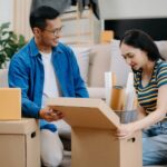 Casal organiza caixas de papelão em uma sala, ilustrando como embalar eletrônicos.